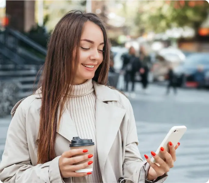 A woman holding a coffee cup while intently looking at her phone, enjoying a moment of relaxation.